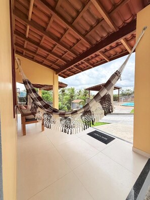 A hammock under a wooden roof, a tiled floor, and a view of a swimming pool. - Pousada Recanto das Orquídeas (Barreirinhas)