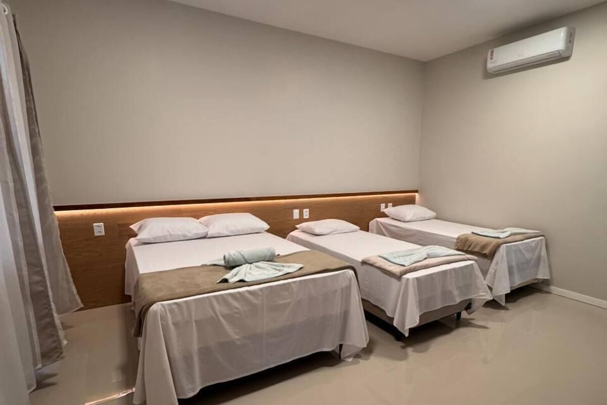 Ein Hotelzimmer mit drei Betten, einem Holzkopfstück, einer weißen Klimaanlage und einem gefliesten Boden.
