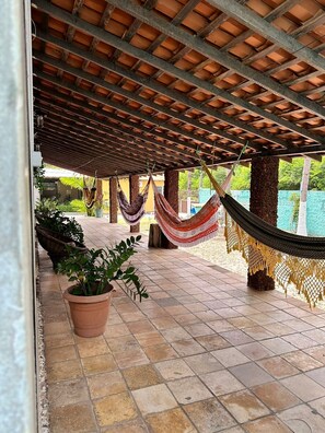 A covered outdoor area with a tiled floor, hammocks, and potted plants. - Pousada Recanto das Orquídeas (Barreirinhas)