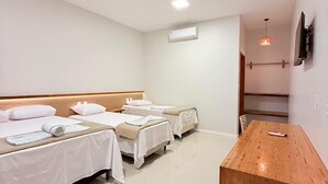 Een hotelkamer met drie bedden, een houten bureau en een aan de muur bevestigde televisie.