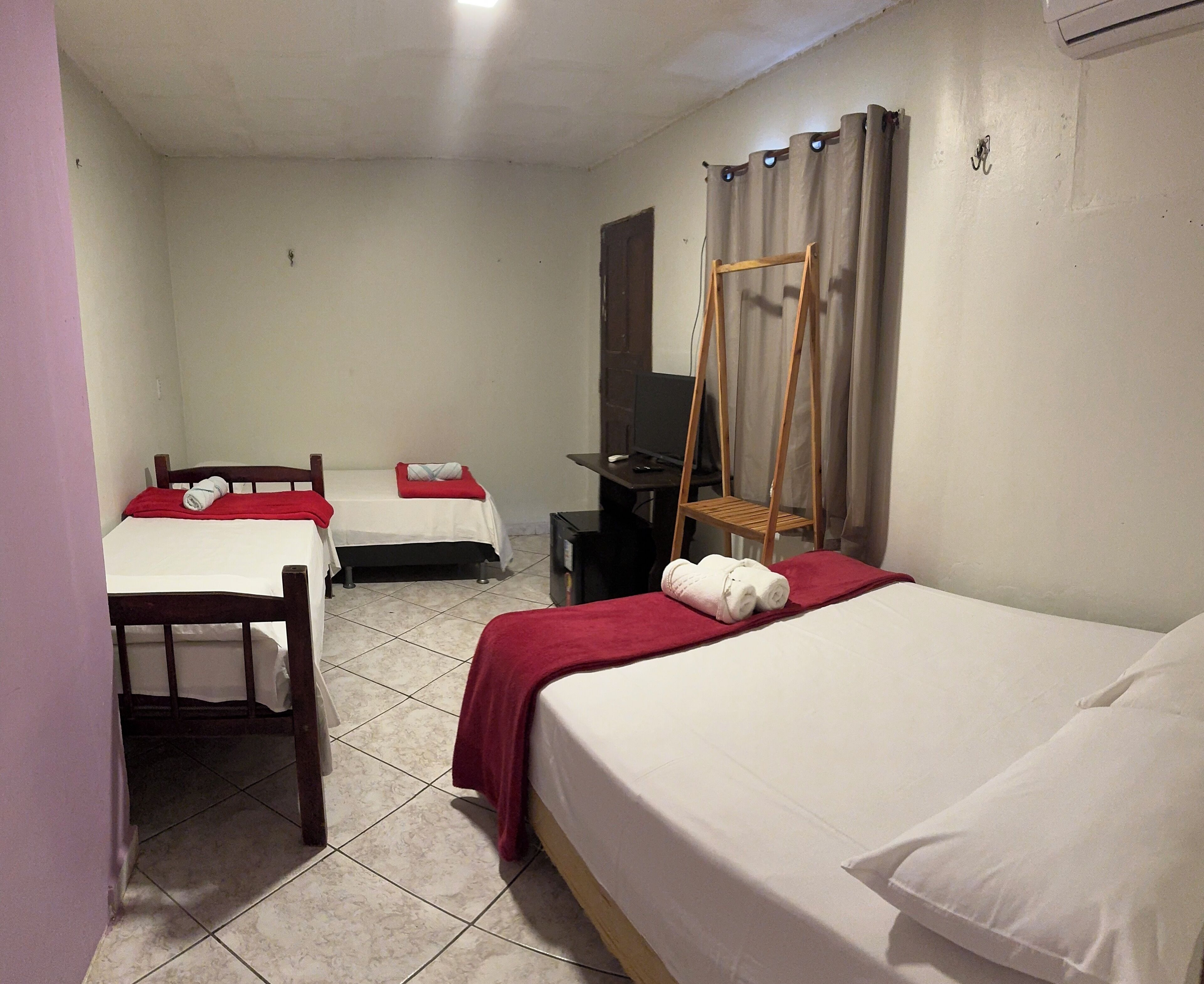Habitación de hotel con dos camas, televisión, una silla de madera y una cortina.