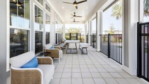 A covered patio with wicker furniture, a central table, ceiling fans, and large windows. - Boho Chic Luxury Retreat Minutes to Theme Parks, Restaurants and Entertainment. (Kissimmee)