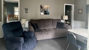 A living room with a brown sofa, a blue armchair, and a small table with a lamp. - Cottage 3 is a charming 2 bedroom 25’ from your boat dock & Hamlin lake. (Ludington)