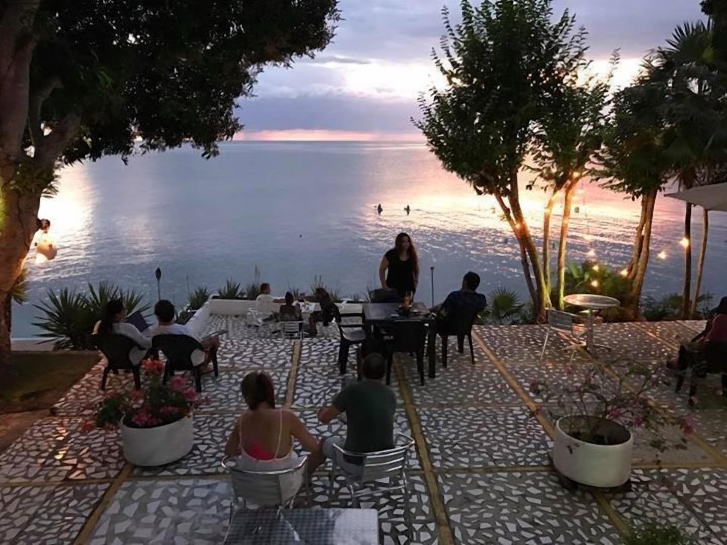 Un espace extérieur aménagé avec des tables, des chaises et des plantes en pot, offrant une vue sur la mer.
