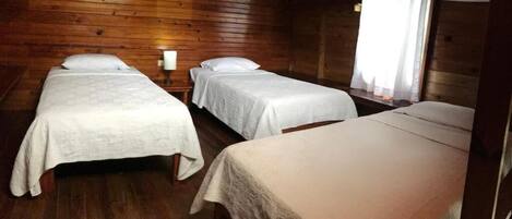 A room with three beds, wooden walls, and a window with curtains.