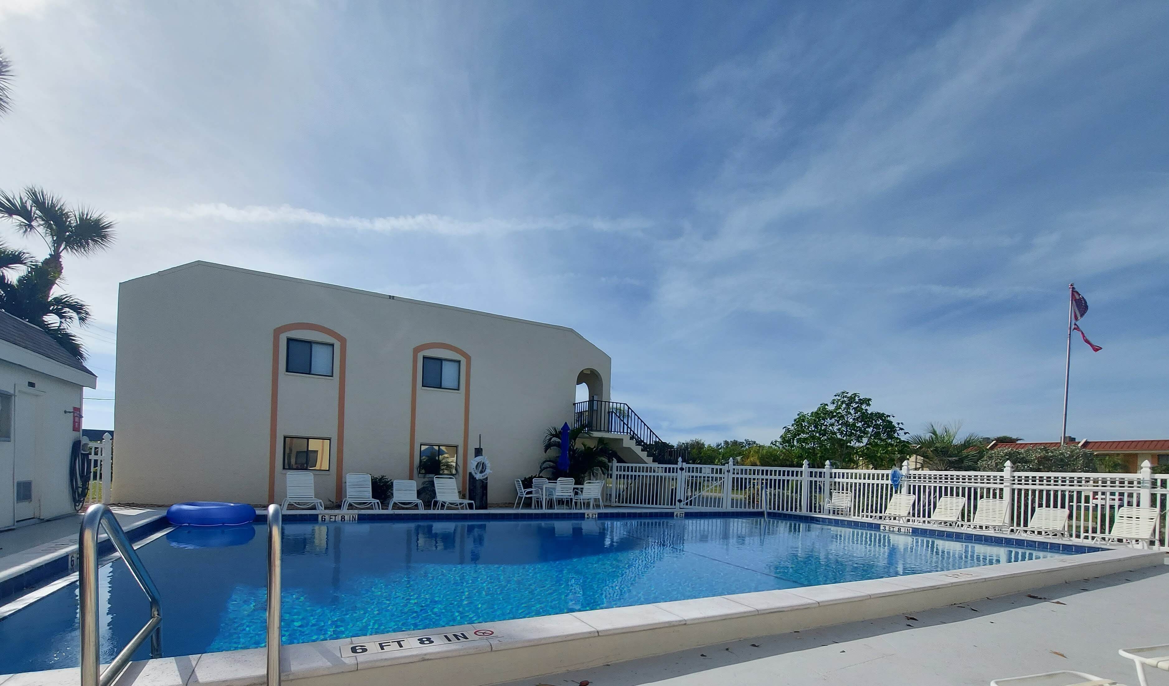 A swimming pool with a 6 ft 8 in depth, adjacent to a building with a white facade and arched windows, and a flagpole with a flag.