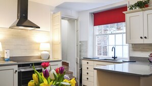 A modern kitchen with white cabinets, a black range hood, a window with a red blind, and a vase of flowers on the counter. - 4 bedroom accommodation in Bridlington (Bridlington)