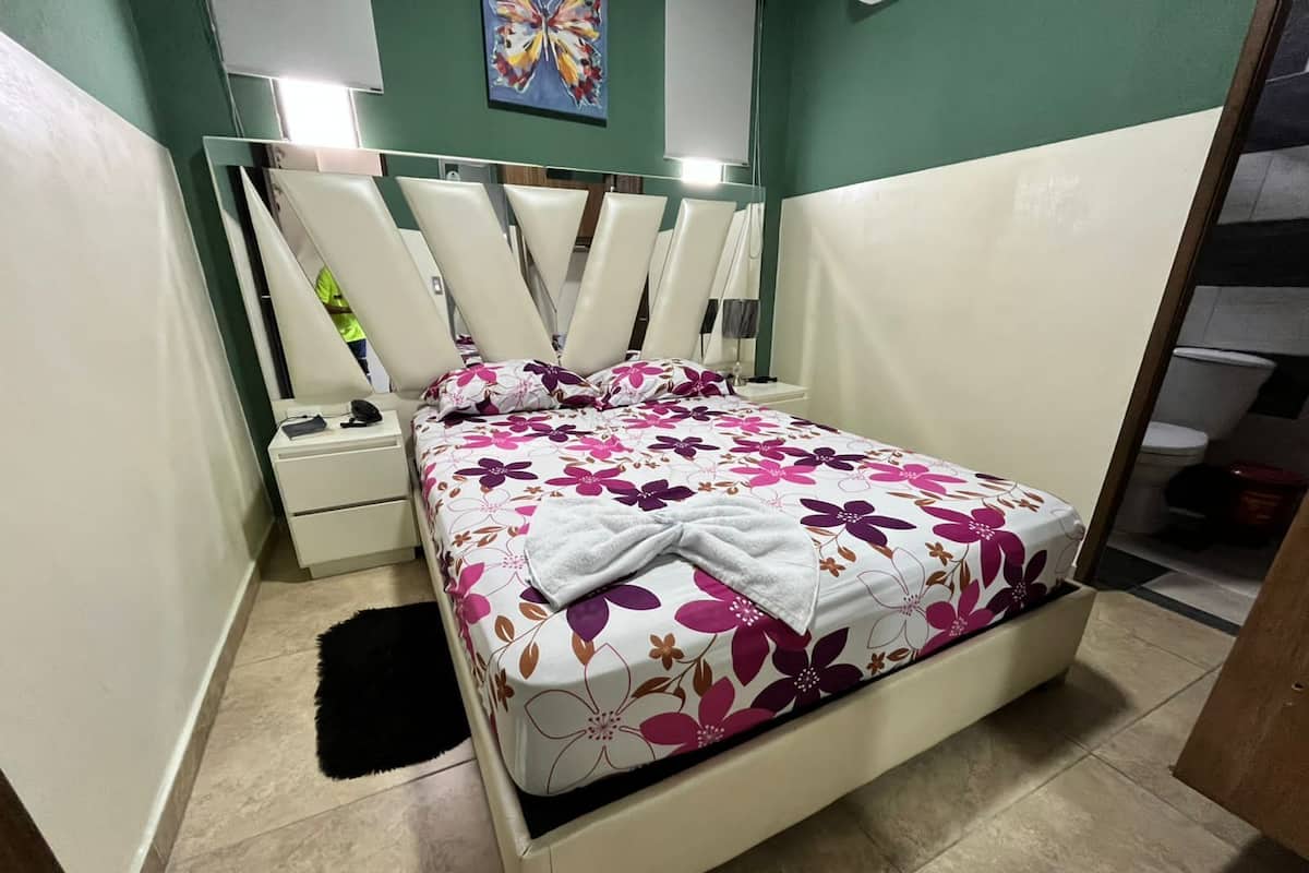Een slaapkamer met een bed, nachtkastjes, een spiegel en een schilderij aan de muur.