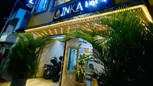 Un hotel de varios pisos con señalización iluminada, una motocicleta estacionada afuera y macetas con plantas en primer plano.