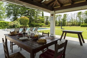 Ein Essbereich im Freien mit Blick auf den Pool, einem Holztisch, Stühlen und einer Bank.