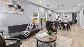A modern living room with a grey sofa, a coffee table, and a dining area with chairs and a table. - Charming Walkable 4 BR/2.5 BA Near Dtown Riverwalk (San Antonio)