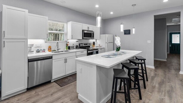 A modern kitchen with white cabinetry, stainless steel appliances, and a central island with bar stools. - Charming Walkable 4 BR/2.5 BA Near Dtown Riverwalk (San Antonio)
