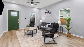 A modern living room with a green door, a ceiling fan, a sofa, a coffee table, and a potted plant. - Charming Walkable 4 BR/2.5 BA Near Dtown Riverwalk (San Antonio)