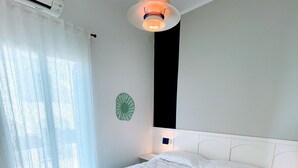 Et soveværelse med en hvid seng, et natbord, en vægmonteret lampe og en grøn pynteting.