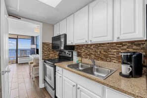 A kitchen with white cabinets, a microwave, stove, and a coffee maker. - Relaxing Oceanfront Condo,Pool,L145 (Myrtle Beach)