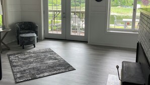 Ein Zimmer mit einer großen Schiebeglasdoor, die auf eine Außenterrasse führt, einem Kamin und einer Wanduhr.