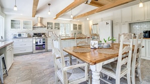 Una cocina amplia con armarios blancos, una mesa de comedor de madera y un alto techo con vigas a la vista.