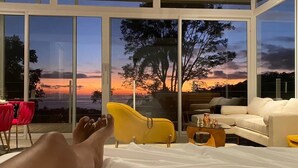 Ein Schlafzimmer mit großem Fenster, einem gelben Sessel, einem weißen Sofa und einem kleinen Tisch.