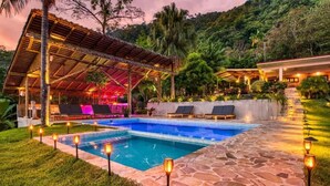 Ein Poolbereich mit Liegestühlen, einer überdachten Lounge und Steinwegen.