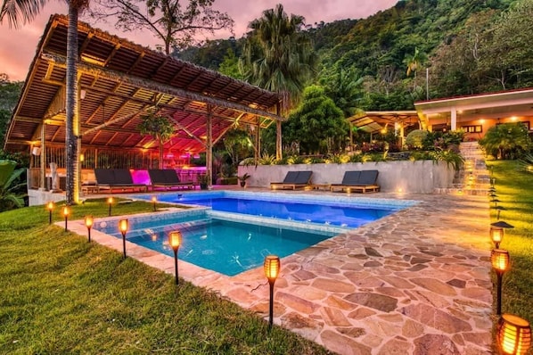 A pool area with lounge chairs, a covered seating area, and stone pathways.