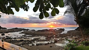 Ein Strand mit Sonnenuntergang, felsigem Ufer und einer Bar mit Getränken.