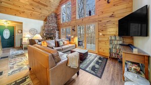 Interior acogedor de una cabaña con chimenea, sofá de cuero, pisos de madera y una estantería.