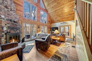A spacious living room with a fireplace, leather sofas, and a large window overlooking a deck.