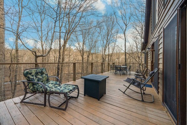A wooden deck with outdoor furniture, including a chair and a table, overlooking a forested area.