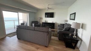 Ein geräumiges Wohnzimmer mit einem großen grauen Sofa, einem kleineren grauen Sessel, einem Couchtisch und einem an der Wand befestigten Fernseher.