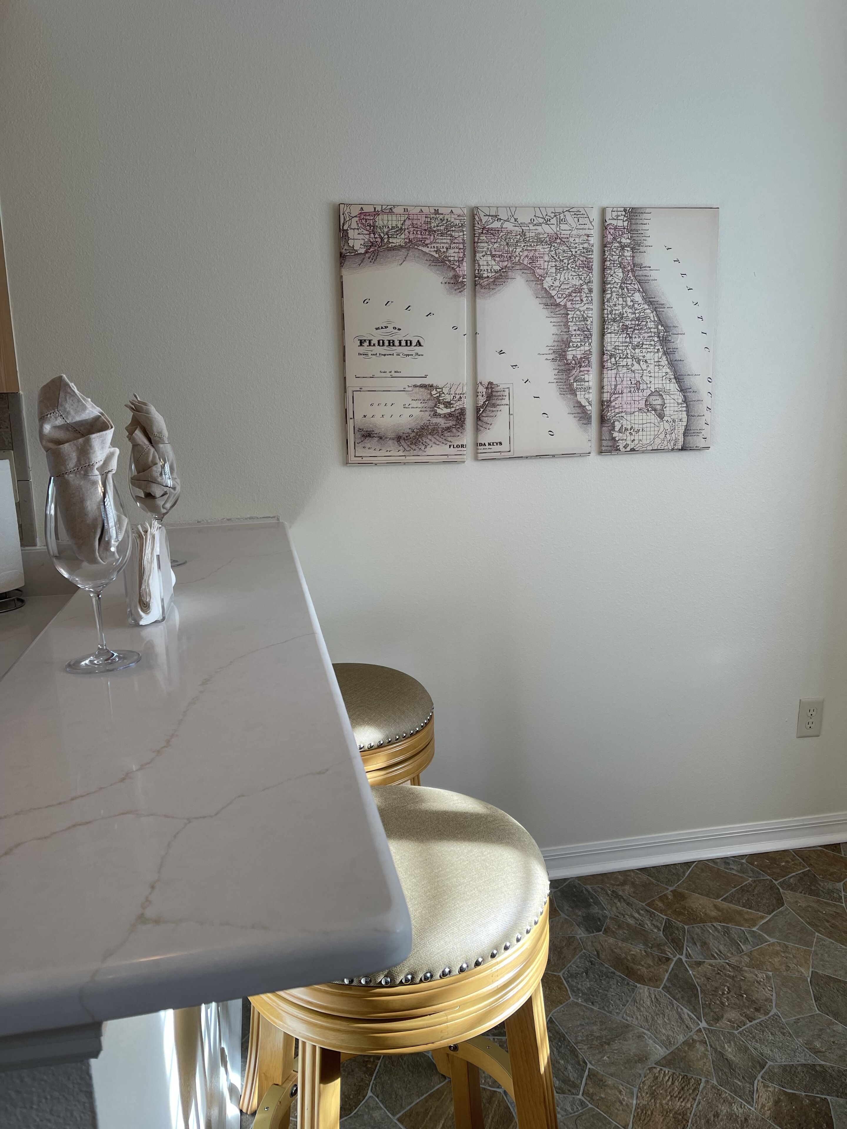 Une cuisine avec un plan de travail en marbre, un tabouret doré et une carte de la Floride accrochée au mur.