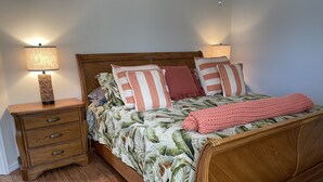 Una cama de madera con una colcha estampada de flores, dos lámparas de noche y una mesita de noche de madera con cajones.