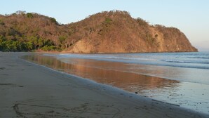 A beach with a curved shoreline, sandy beach, and a hill with sparse vegetation.