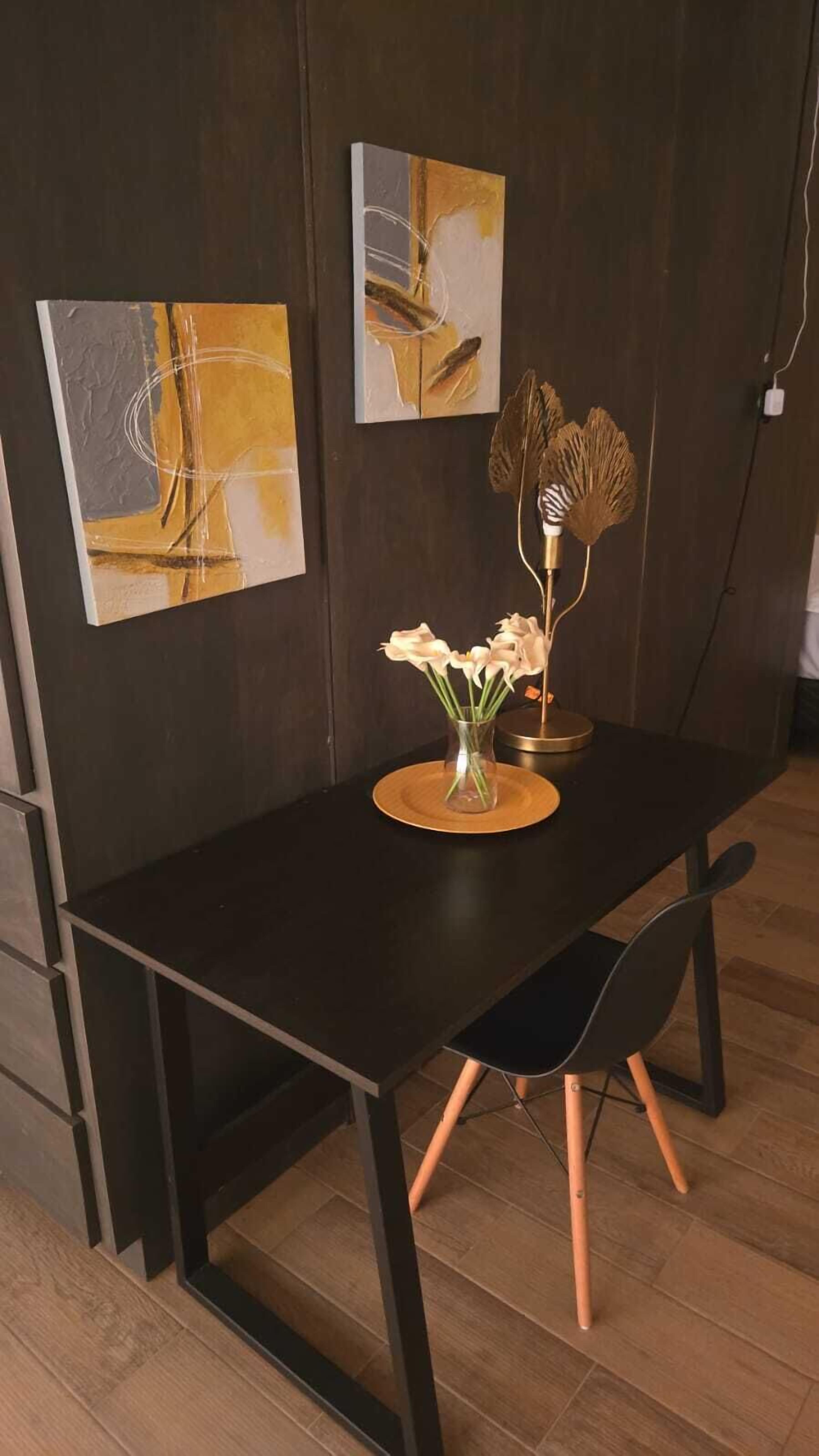 A dining area with a dark wooden table, a vase with white flowers, and abstract art on the wall.