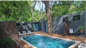 A swimming pool with lounge chairs, a wooden deck, and a tree.