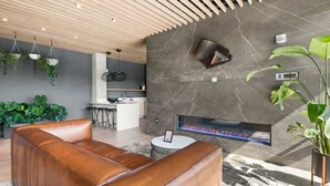 A modern living room with a fireplace, leather sofa, and hanging plants.