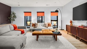 A modern living room with a sofa, ottoman, and a flat-screen TV.