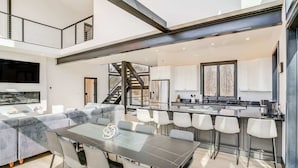 A modern kitchen with a central island, a dining area with a table and chairs, and a staircase leading to an upper level. - Lux Mountain Retreat w/ Heated Indoor Pool (Windham)
