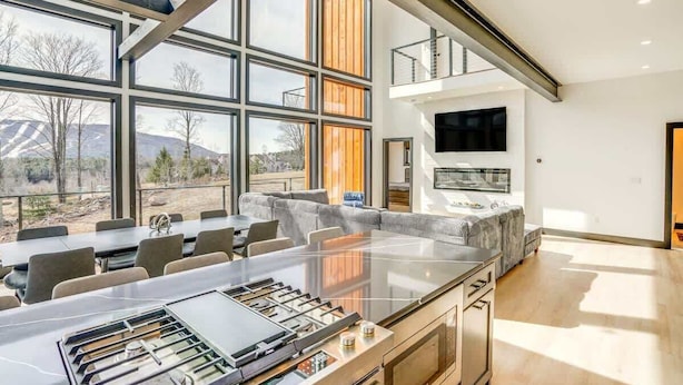 A modern kitchen with a large island, large windows, and a flat-screen TV. - Lux Mountain Retreat w/ Heated Indoor Pool (Windham)