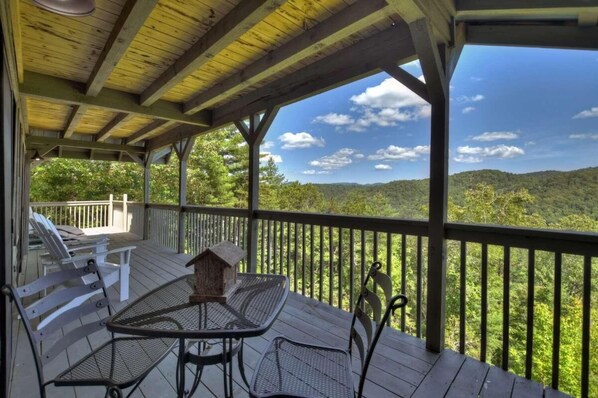 A covered outdoor deck with a table and chairs, overlooking a forested landscape.