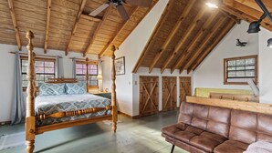 Un dormitorio amplio con una cama de madera grande, un sofá de cuero y un techo inclinado con vigas a la vista.