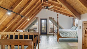 Un dormitorio acogedor en el ático, con techo de madera, cama con dosel, escritorio y vistas al exterior.