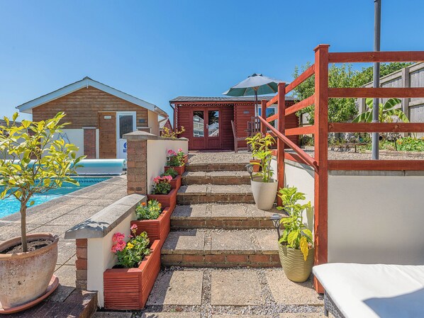 A poolside area with steps leading to a wooden building, potted plants, and a clear blue sky.