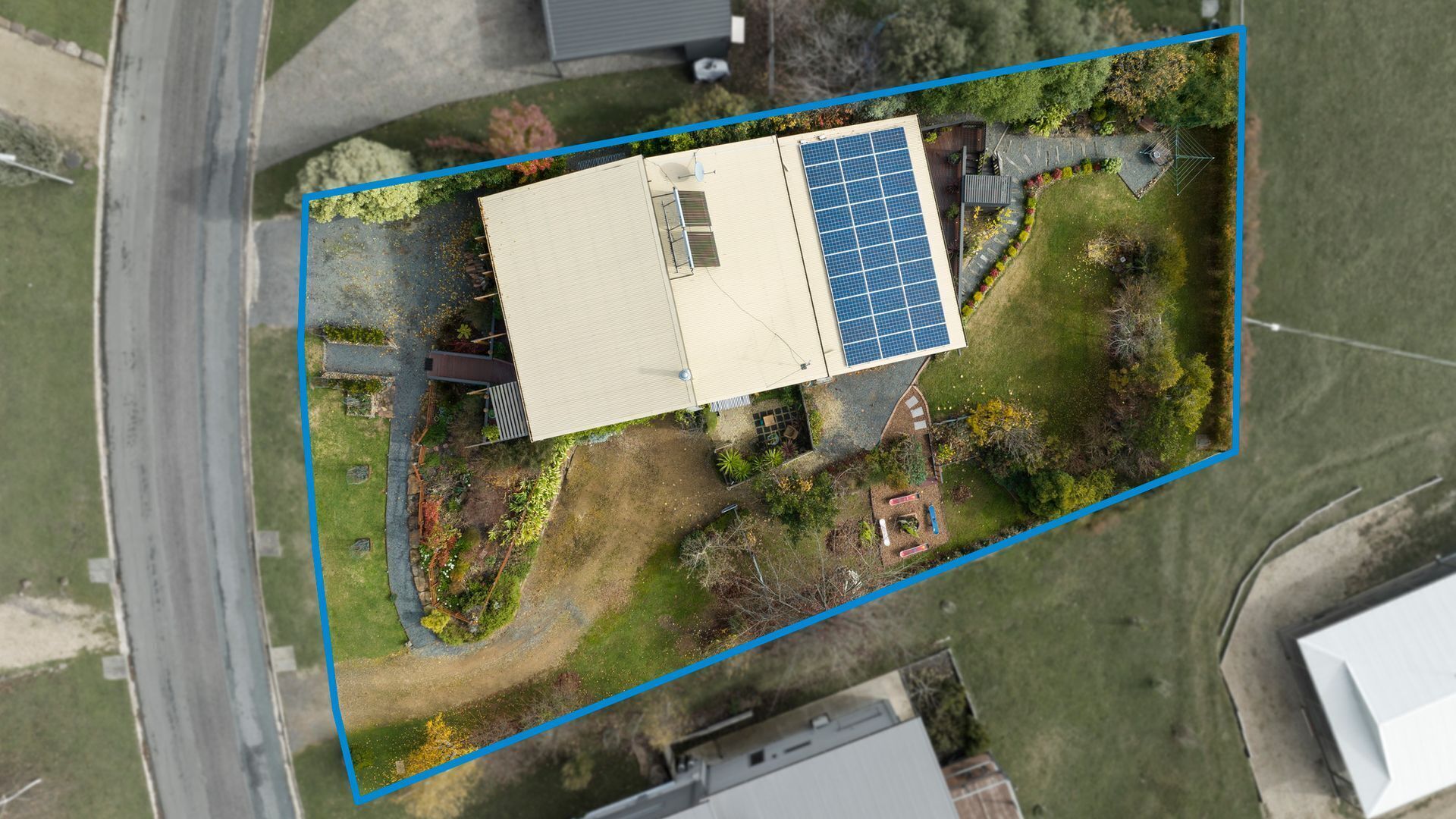 Vista aérea de una propiedad residencial con un panel solar, un jardín cercado y un camino de entrada.