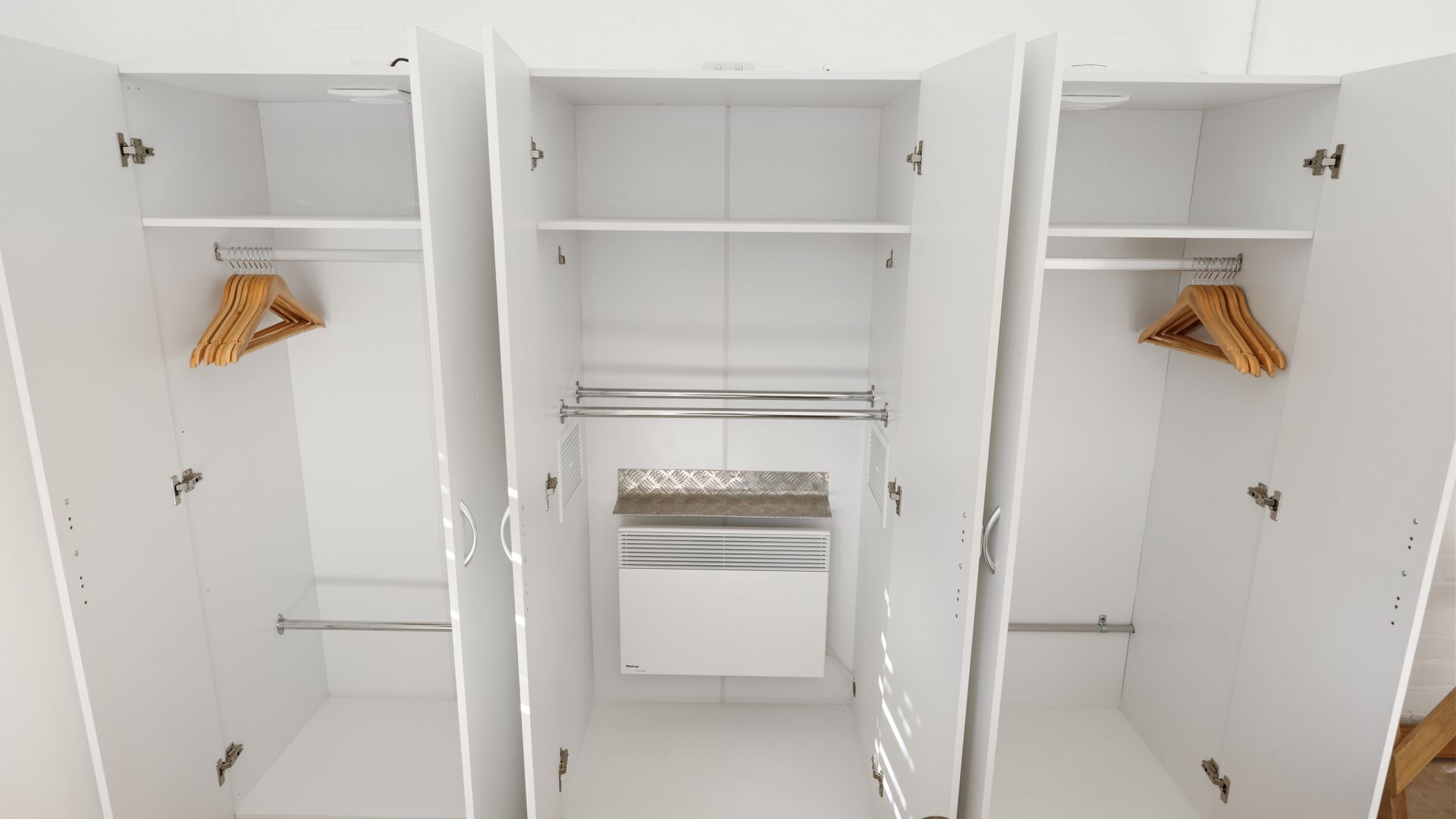 A white walk-in closet with multiple shelves, a hanging rod, and a built-in heater.