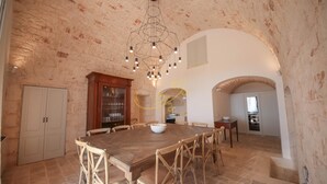 Ein geräumiger Essbereich mit großem Holztisch und Korbstühlen, einem modernen Kronleuchter und einer durch einen Bogen sichtbaren Küche.