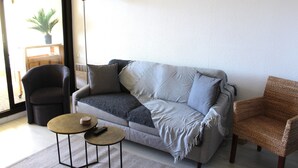A living room with a grey sofa, a small round table, a wicker chair, and a tall floor lamp. - Les Terrasses de Cassis (Cassis)