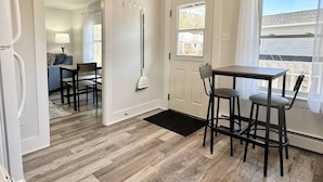Una habitación con piso de madera, una mesa de comedor con dos sillas, una puerta y una ventana con cortinas.
