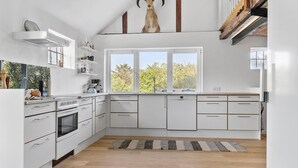 Una cocina moderna con armarios blancos, horno empotrado y un amplio ventanal con vista a una calle arbolada.