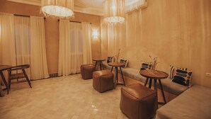 A spacious living area with a sofa, ottomans, a coffee table, and a dining table. - Riad Villa Amood (Taouz)