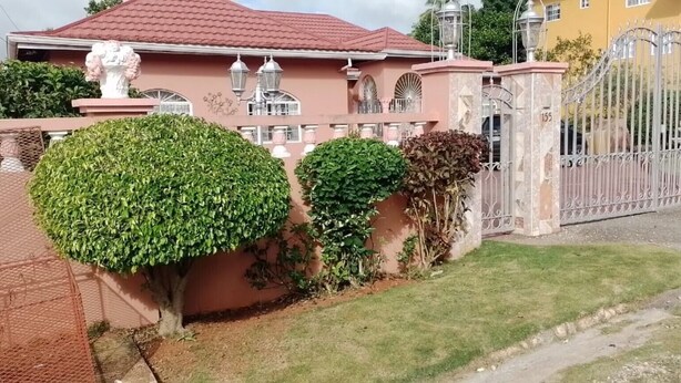 Un lotissement résidentiel fermé, avec une maison rose, une pelouse bien entretenue et un portail en métal.